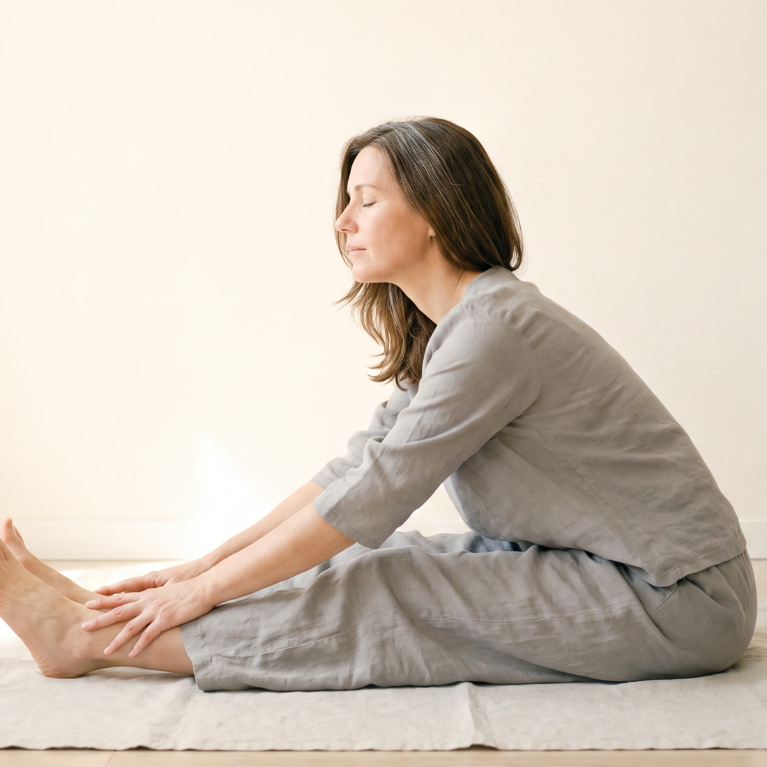 A woman stretching gently on a mat in soft light.