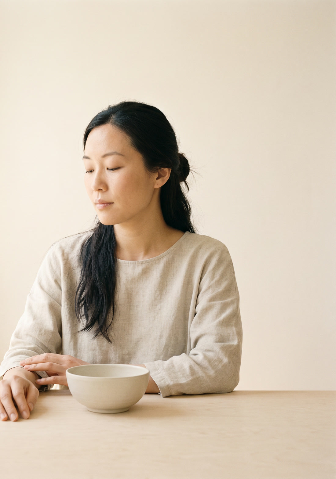 A woman at a table with a bowl, unhurried, in soft light.
